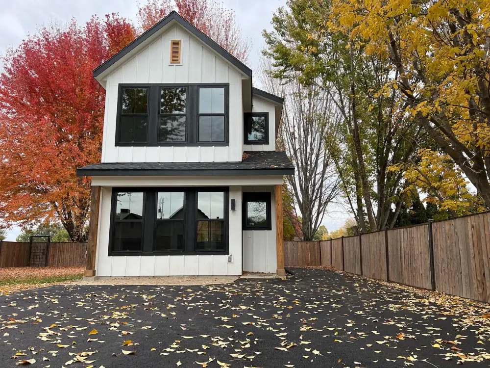 Two-story white board-and-batten farmhouse with black window trim and Idaho landscape in autumn